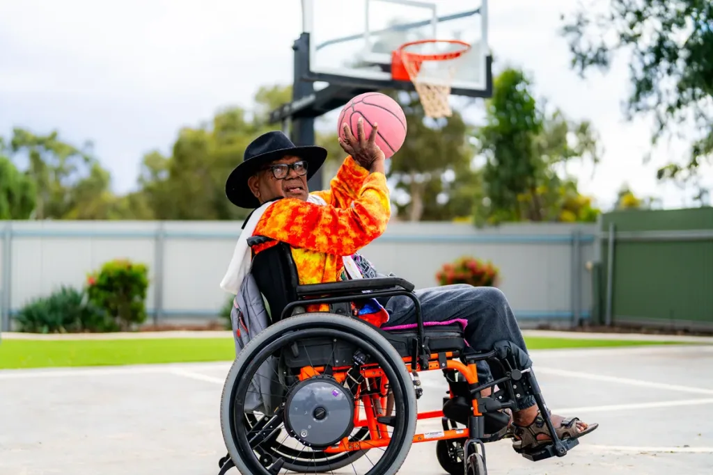 A participant in a wheelchair shooting a basketball on the Activity Hub court
