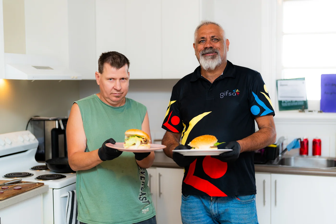 A participant and a GIFSA support worker holding up the burgers they made together