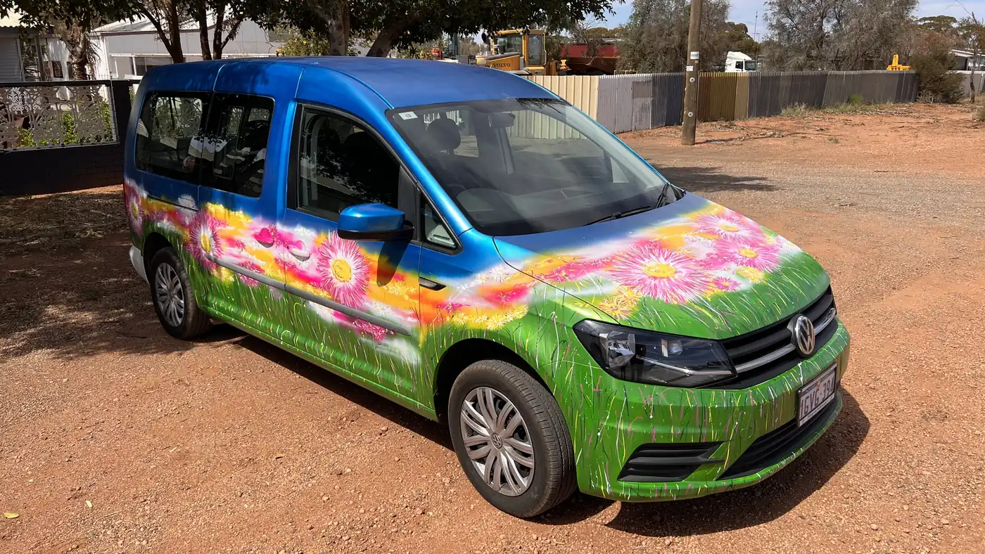 A GIFSA van painted with bright flowers, parked on red dirt