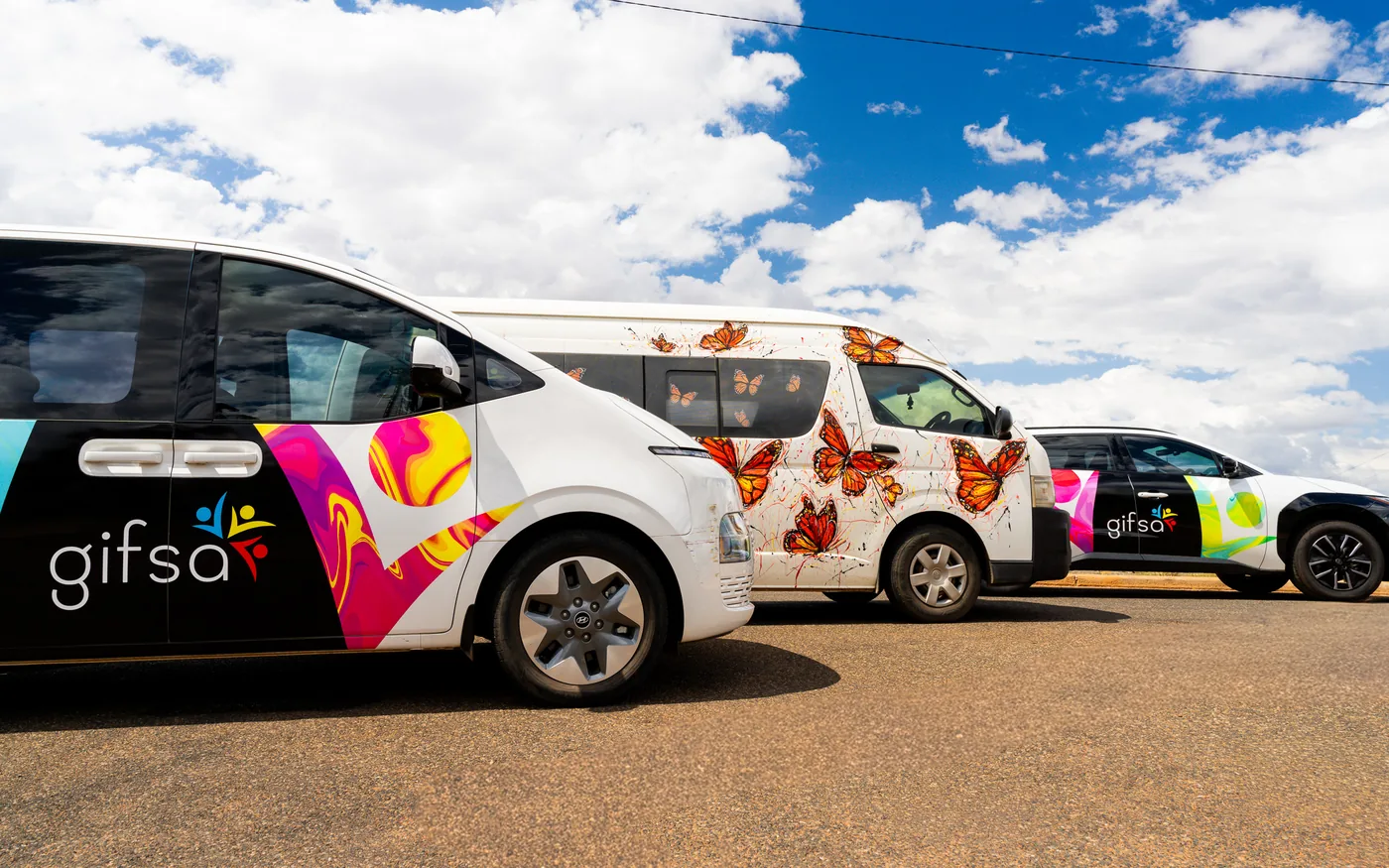 Three GIFSA vehicles with butterfly and colourful artwork parked in a row
