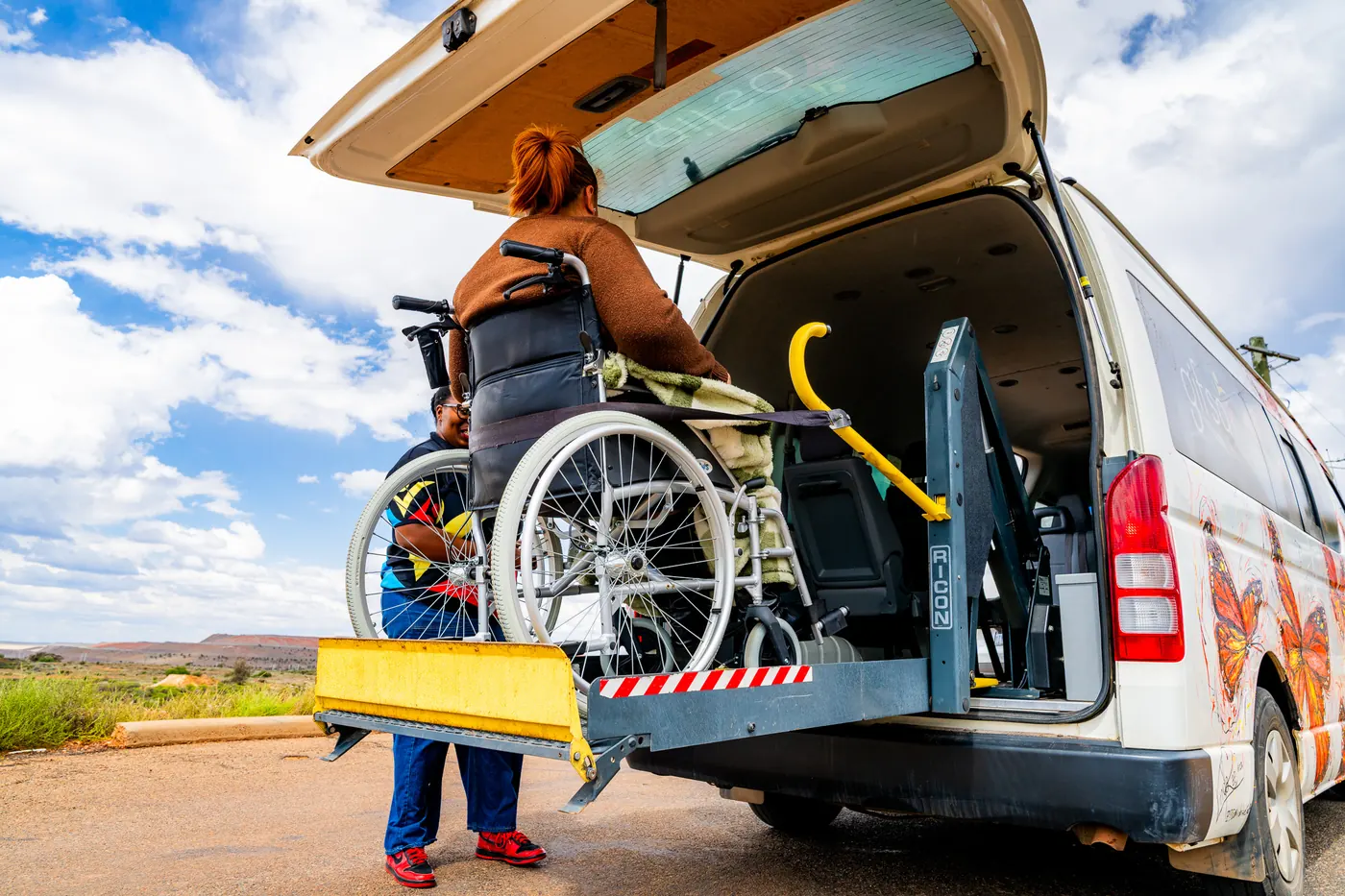 A participant in a wheelchair on the lift of a GIFSA accessible van