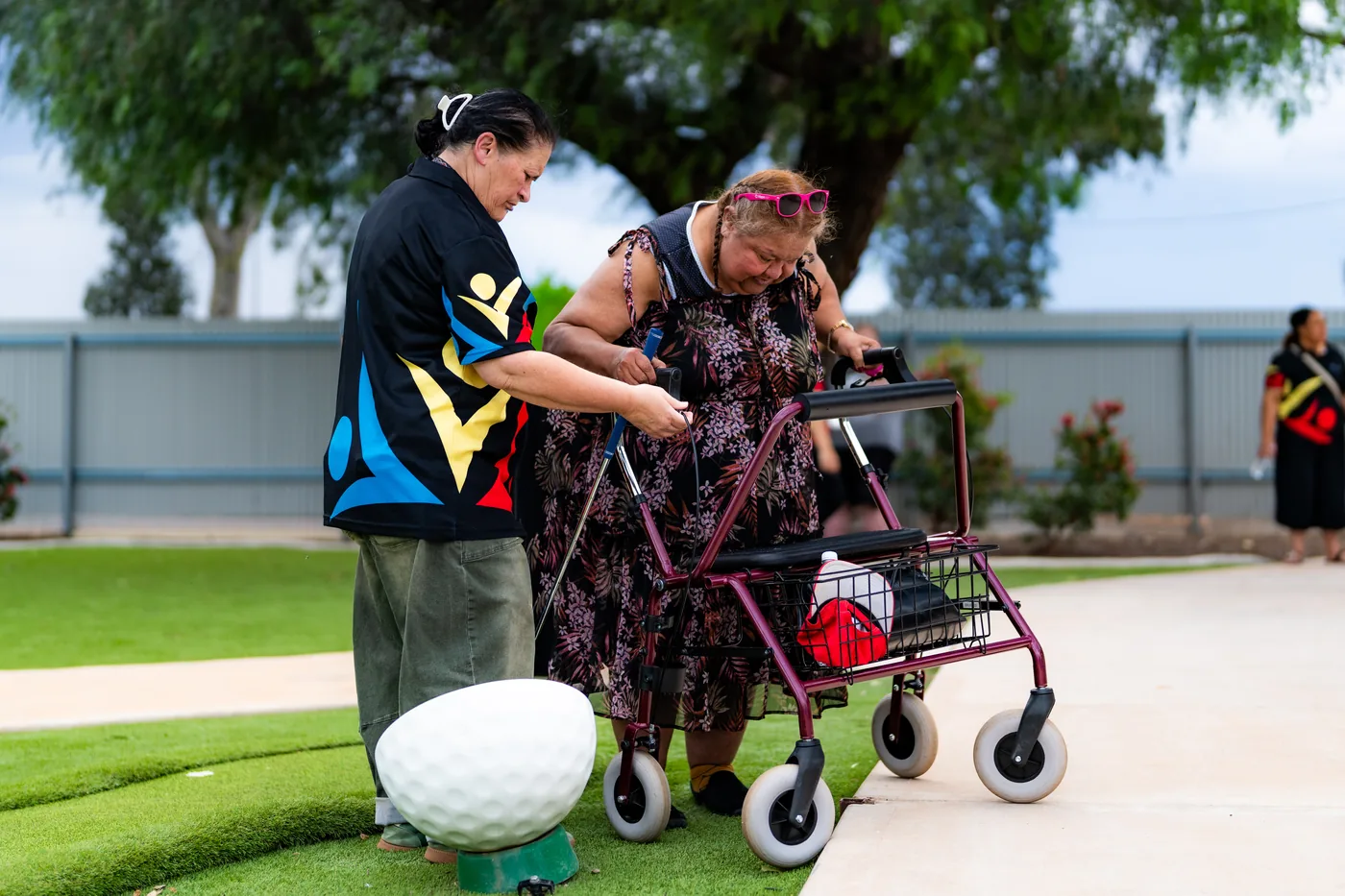 A GIFSA support worker helps a participant with a walking frame line up a putt on the mini golf course