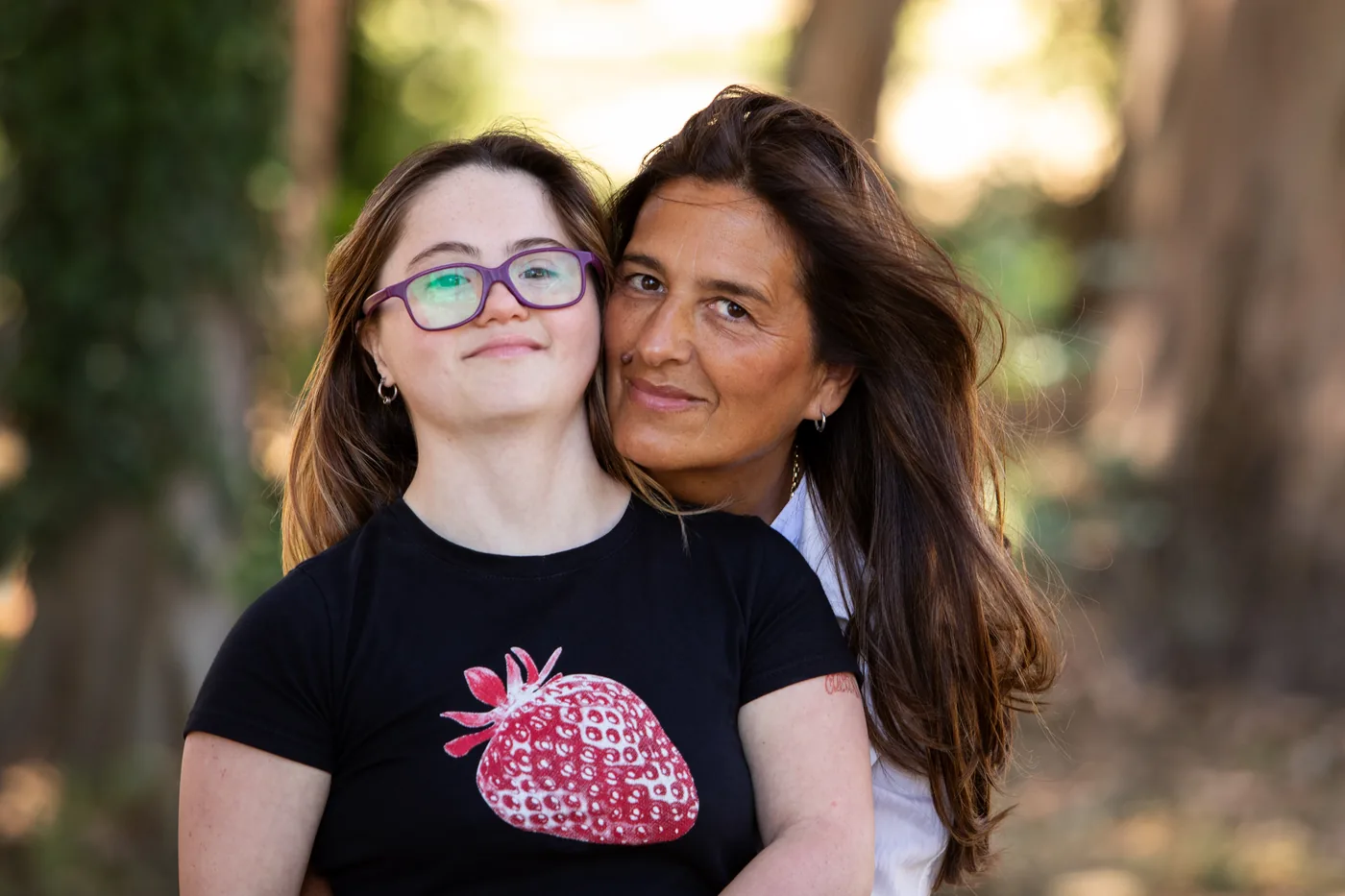 A smiling mother hugging her teenage daughter outdoors